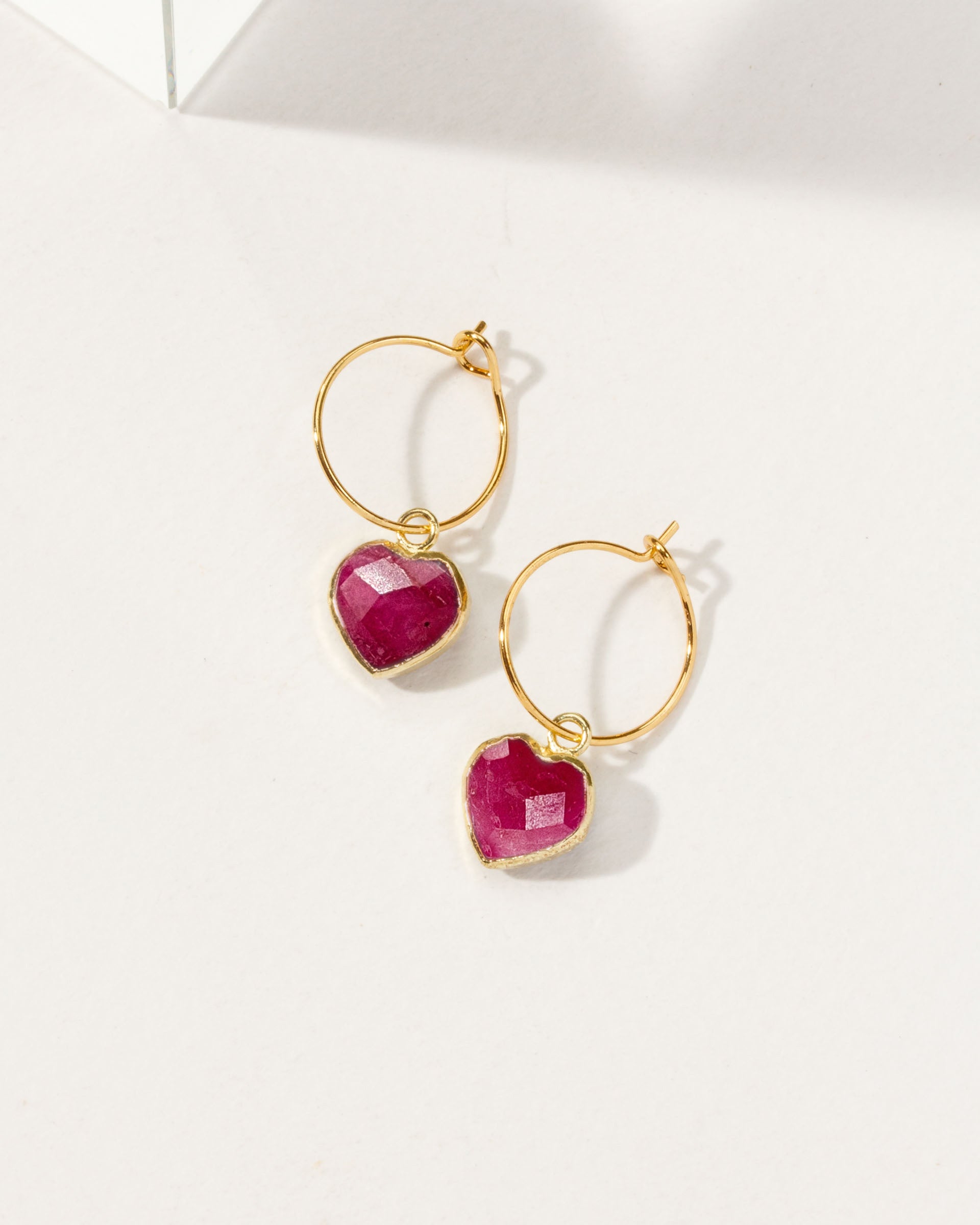 Gold hoop earrings with red ruby gemstones on a white background