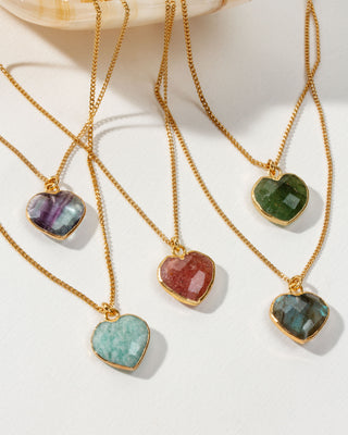 A collection of heart-shaped gemstone gold chain necklaces in various colors, displayed on a white surface.