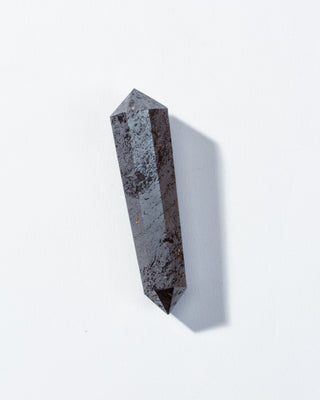A double-pointed hematite gemstone with a metallic shine and sharp faceted edges on a white background.