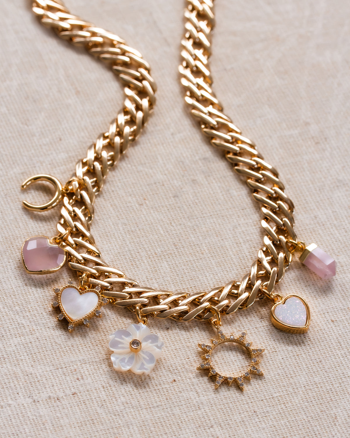 A chunky gold chain charm necklace with rose quartz, mother-of-pearl, and druzy charms
