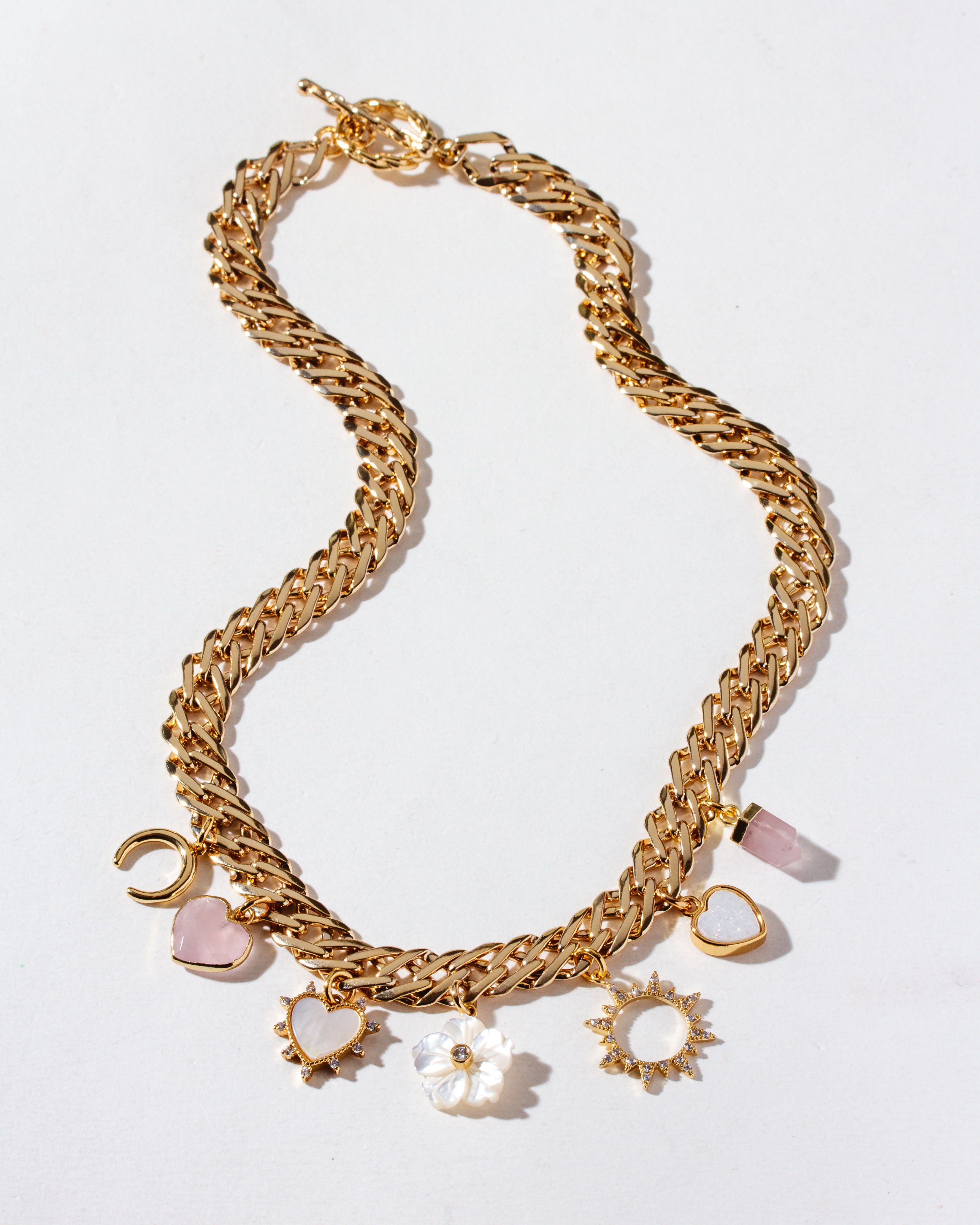 A chunky gold chain charm necklace with rose quartz, mother-of-pearl, and druzy charms