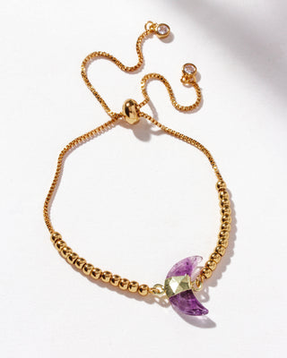 Gold adjustable bracelet with a crescent moon-shaped genuine amethyst stone centerpiece, cz crystals, and small gold beads on a white background.