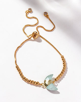 Gold adjustable bracelet with a crescent moon-shaped genuine aquamarine stone centerpiece, cz crystals, and small gold beads on a white background.