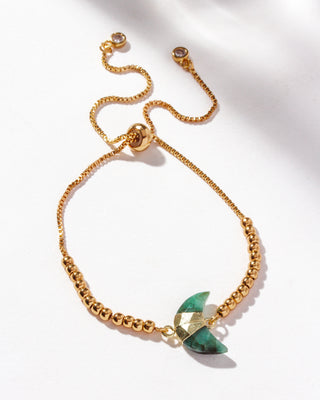 Gold adjustable bracelet with a crescent moon-shaped genuine emerald stone centerpiece, cz crystals,  and small gold beads on a white background.