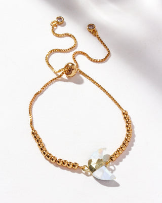A gold adjustable bracelet with a crescent moon-shaped genuine moonstone stone centerpiece, cz crystals, and small gold beads on a white background.