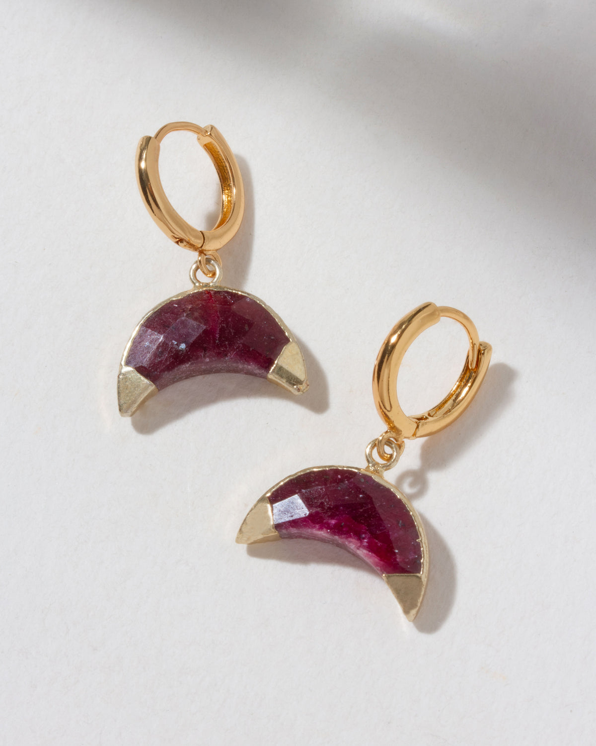 Tow Gold hoop earrings with ruby gemstone half-moon pendants on a light background