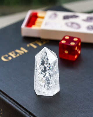 Quartz mini tower obelisk sitting on a black book with a red die and matchbook in the background.