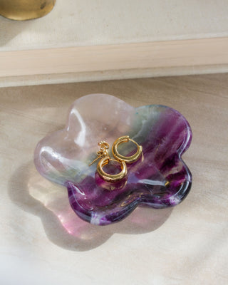 A daisy-shaped fluorite gemstone jewelry catchall dish with a unique color pattern, containing gold-colored earrings on a white surface.