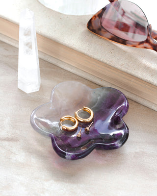 A daisy-shaped fluorite gemstone jewelry catchall dish with a unique color pattern, containing gold-colored earrings on a white surface.