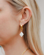 Close up of woman wearing diamond card suite charm gold earring in mother of pearl