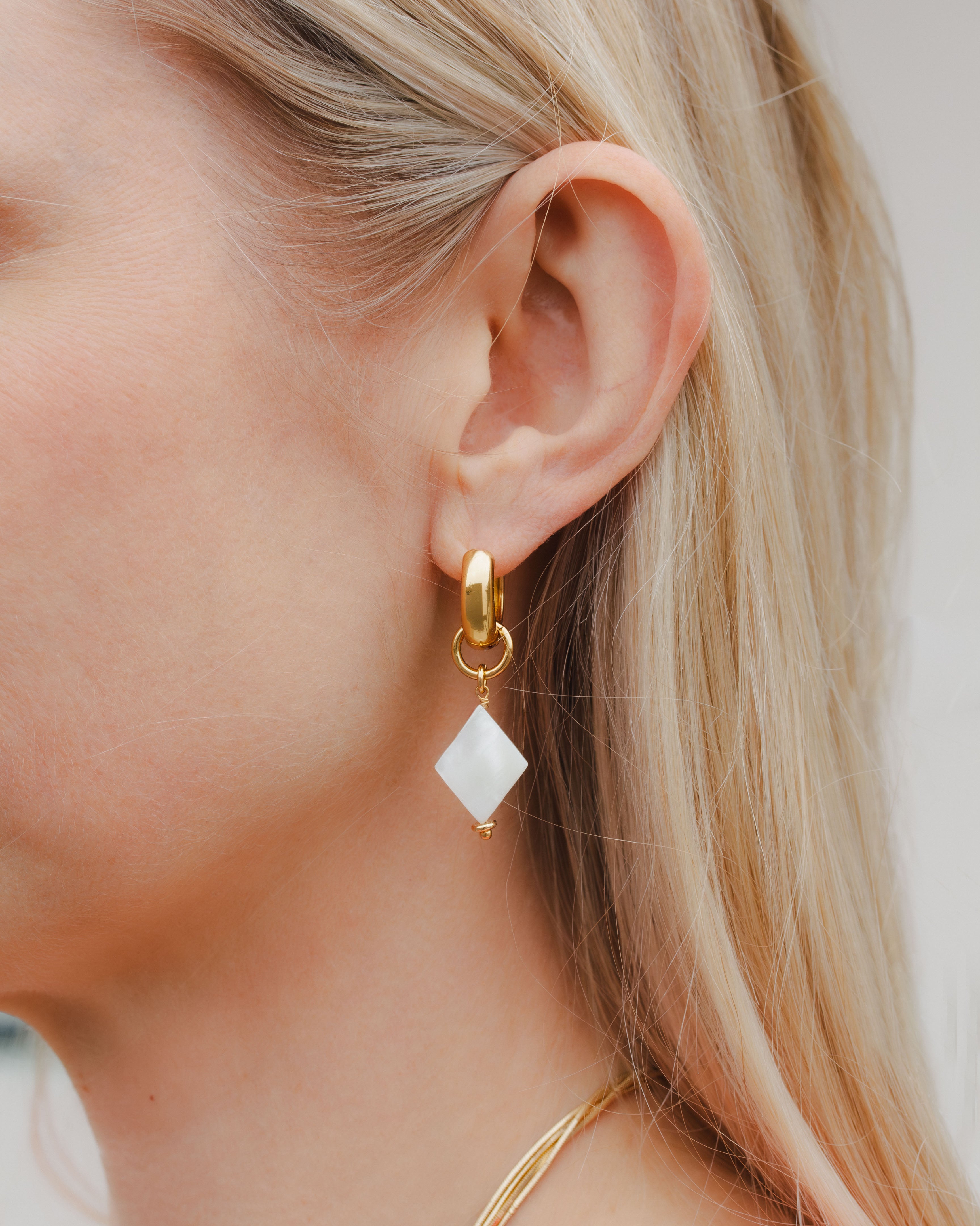 Close up of woman wearing diamond card suite charm gold earring in mother of pearl