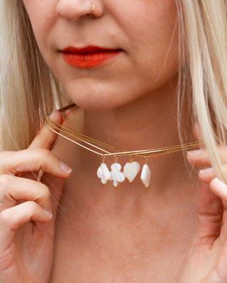 Woman wearing gold layered necklace with diamond, spade, club, and heart card suite mother of pearl charms.
