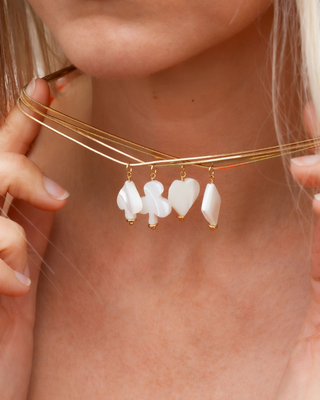 Gold necklace with heart, spade, diamond, and clubs card suites shaped pendants worn by a woman.