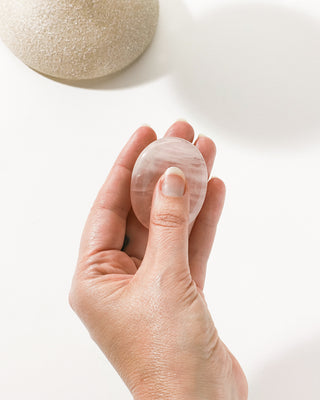 Close up of model holding a smooth rose quartz ‘don’t you stone’ against the white background.