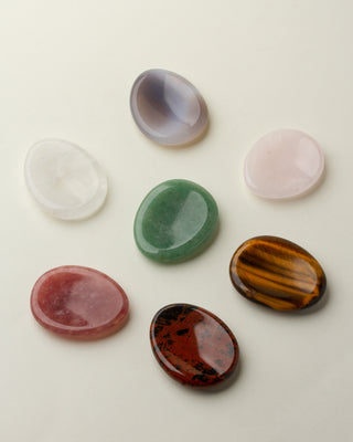 A collection of smooth polished stones arranged on a light surface, showcasing a variety of colors including white, pink, green, red, and brown.