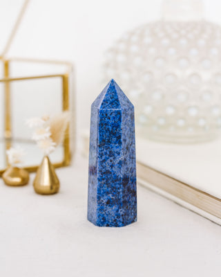A polished dumortierite crystal tower with rich, denim-blue tones and natural variations, displayed on a white surface.