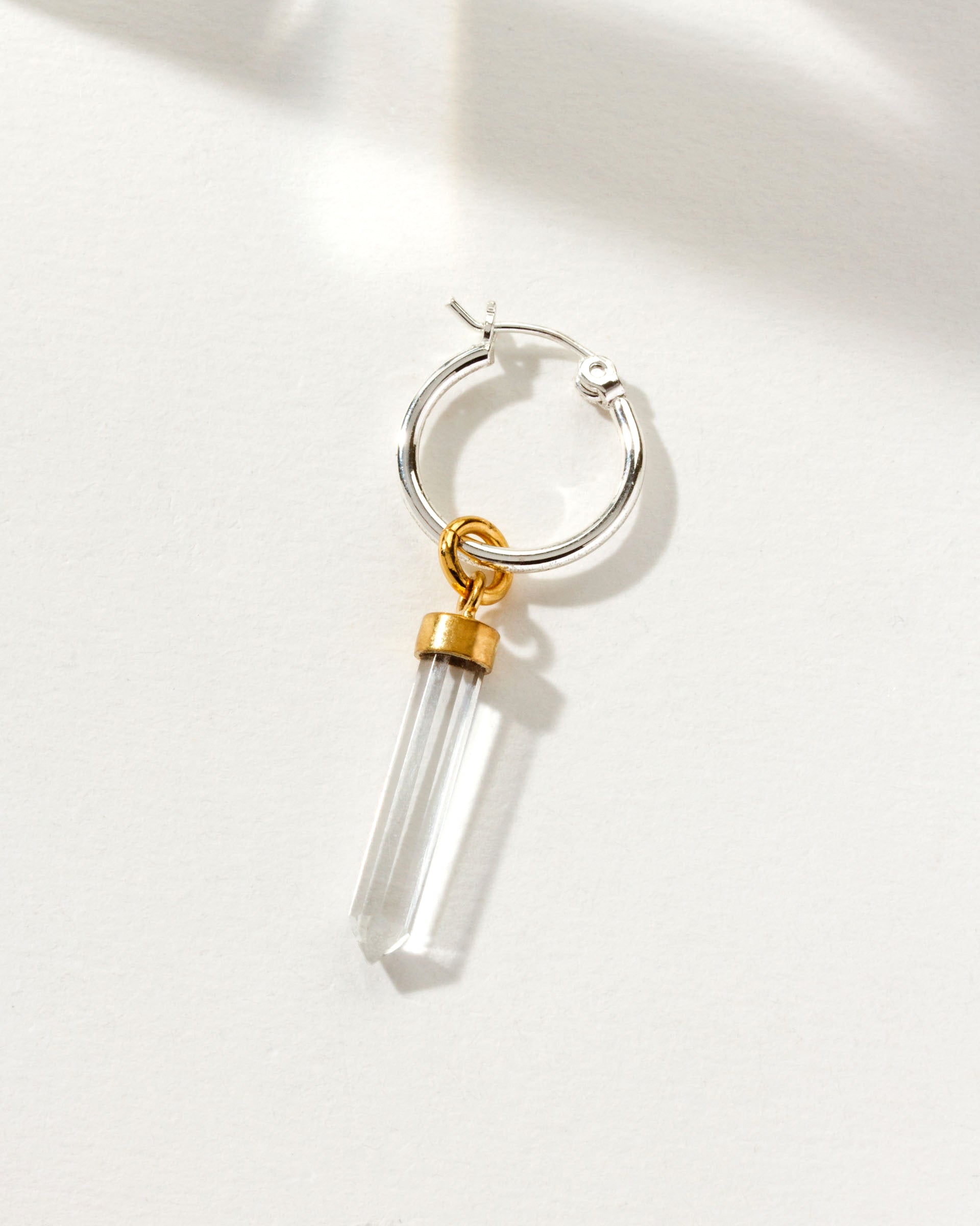 Silver hoop earring with a clear quartz-like charm and gold accents.