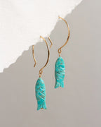 Turquoise fish-shaped earrings on gold hooks against a light gray background