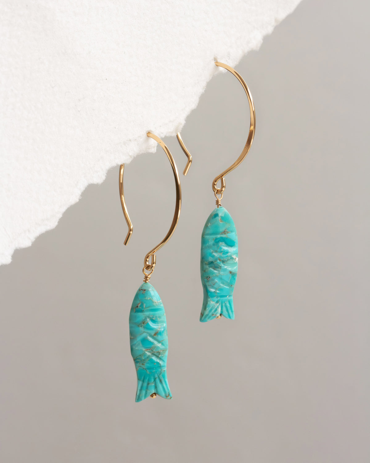Turquoise fish-shaped earrings on gold hooks against a light gray background