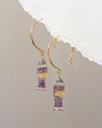Gold earrings with multicolored gemstones on a gray background