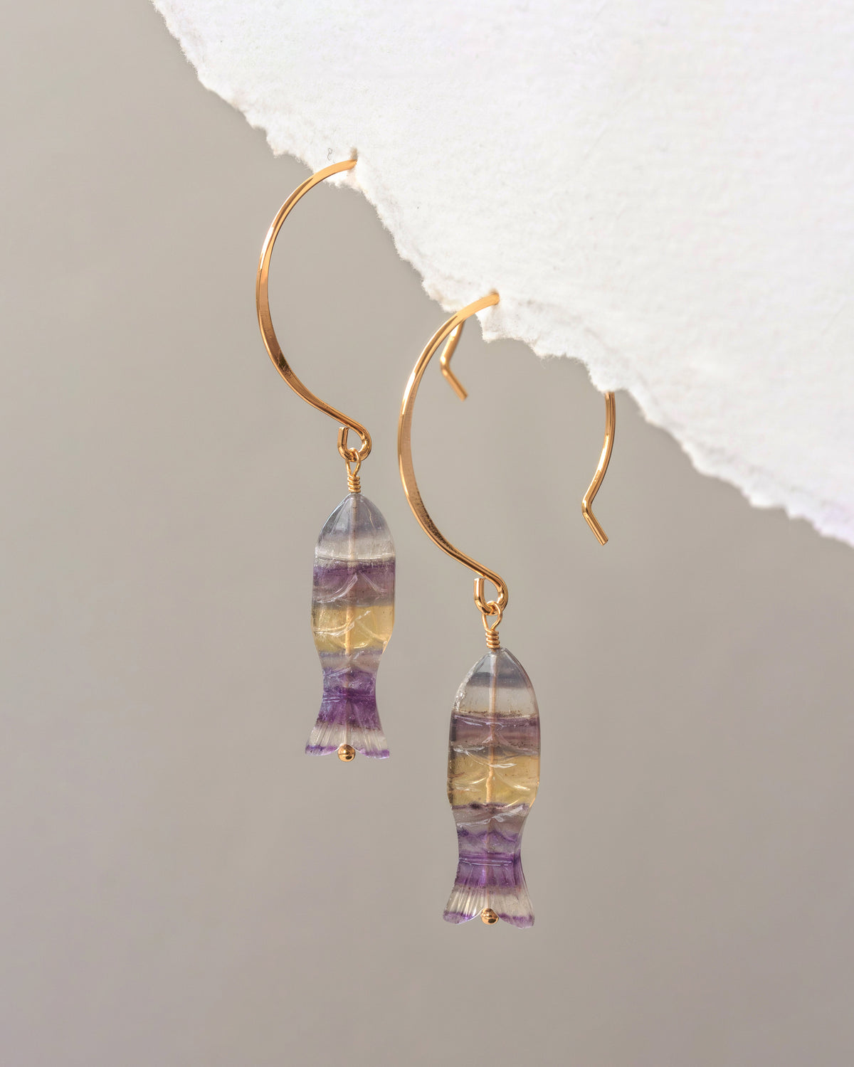 Gold earrings with multicolored gemstones on a gray background