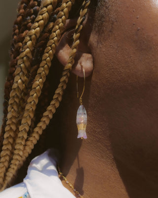 Close-up of a person wearing a gold earring with a clear gemstone, against a blurred background.