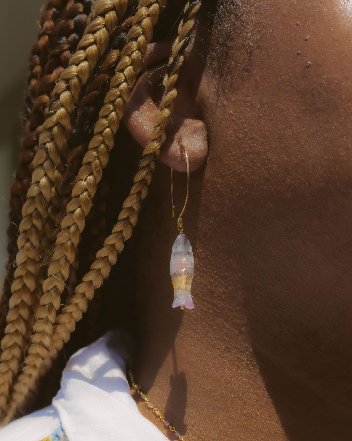 Close-up of a person wearing a gold earring with a clear gemstone, against a blurred background.