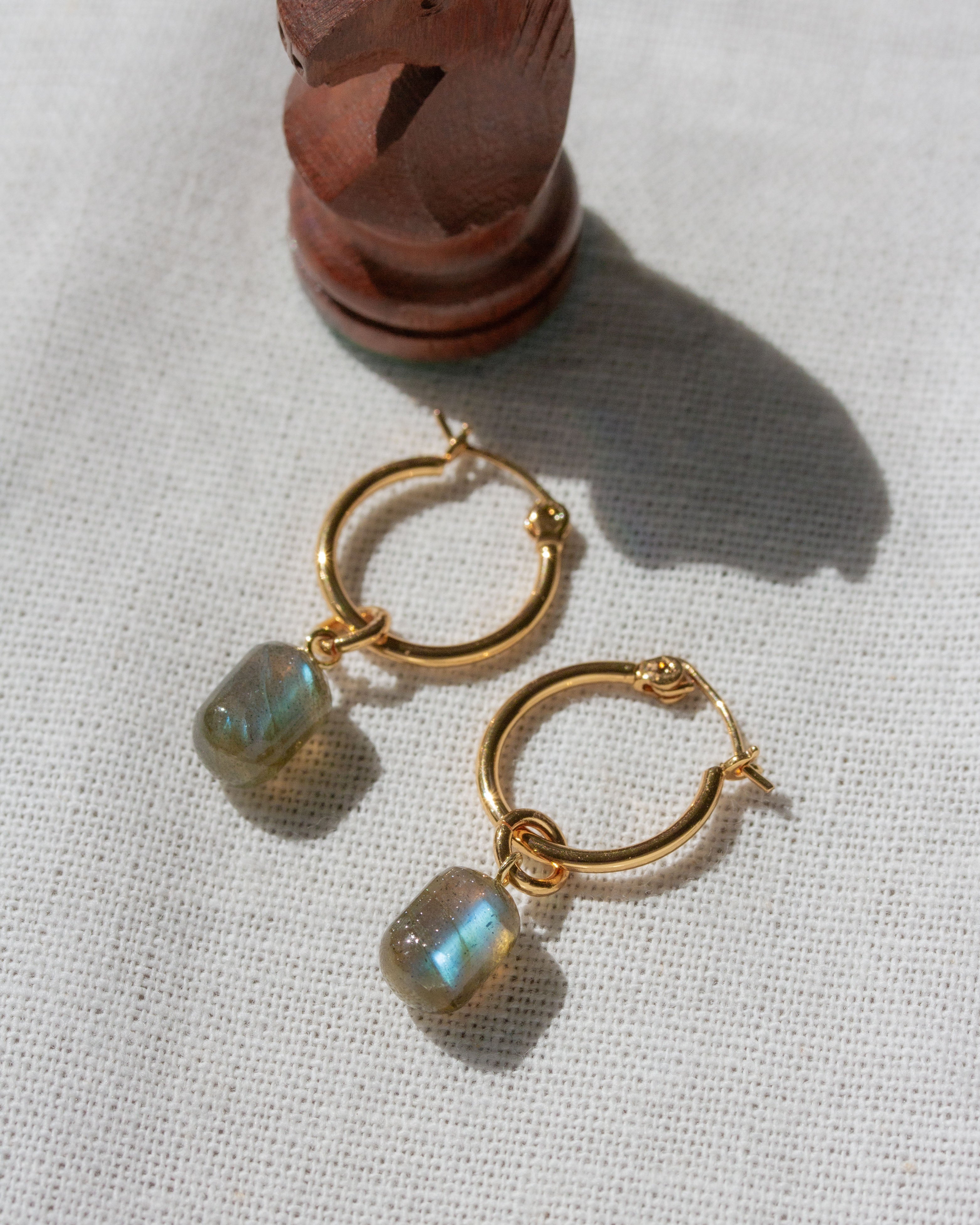 Gold Pill Drop Hoop Earrings with Labradorite gemstones next to a chess piece.