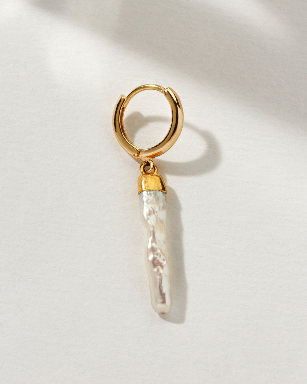 A gold hoop earring with a dangling, elongated pearl.