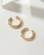 Two gold "Sleek Orbit Ear Cuffs" are on a white surface with geometric shadows.