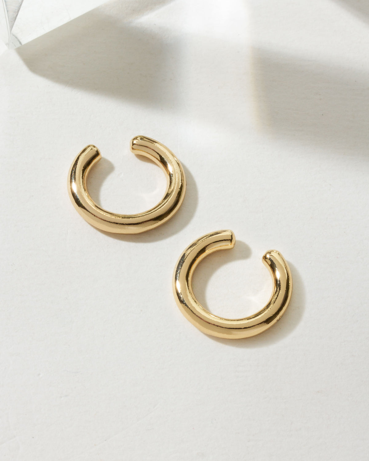 Two gold "Sleek Orbit Ear Cuffs" are on a white surface with geometric shadows.