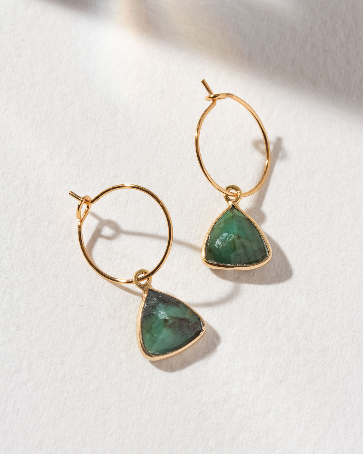 Two Bermuda Triangle Mini Hoops with Emerald stones and gold hoops are displayed.