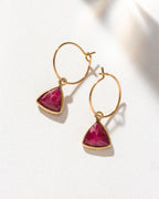 Gold mini hoops with a triangular Ruby gemstone charm are displayed.