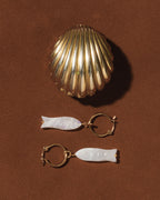 Gold and white fish-shaped earrings on a brown background