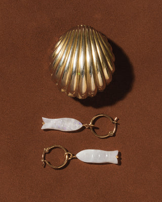 Gold and white fish-shaped earrings on a brown background