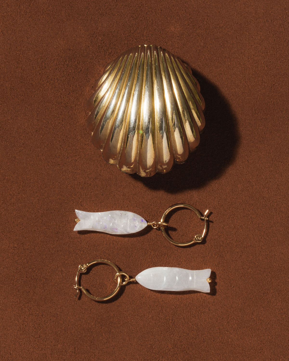 Gold and white fish-shaped earrings on a brown background