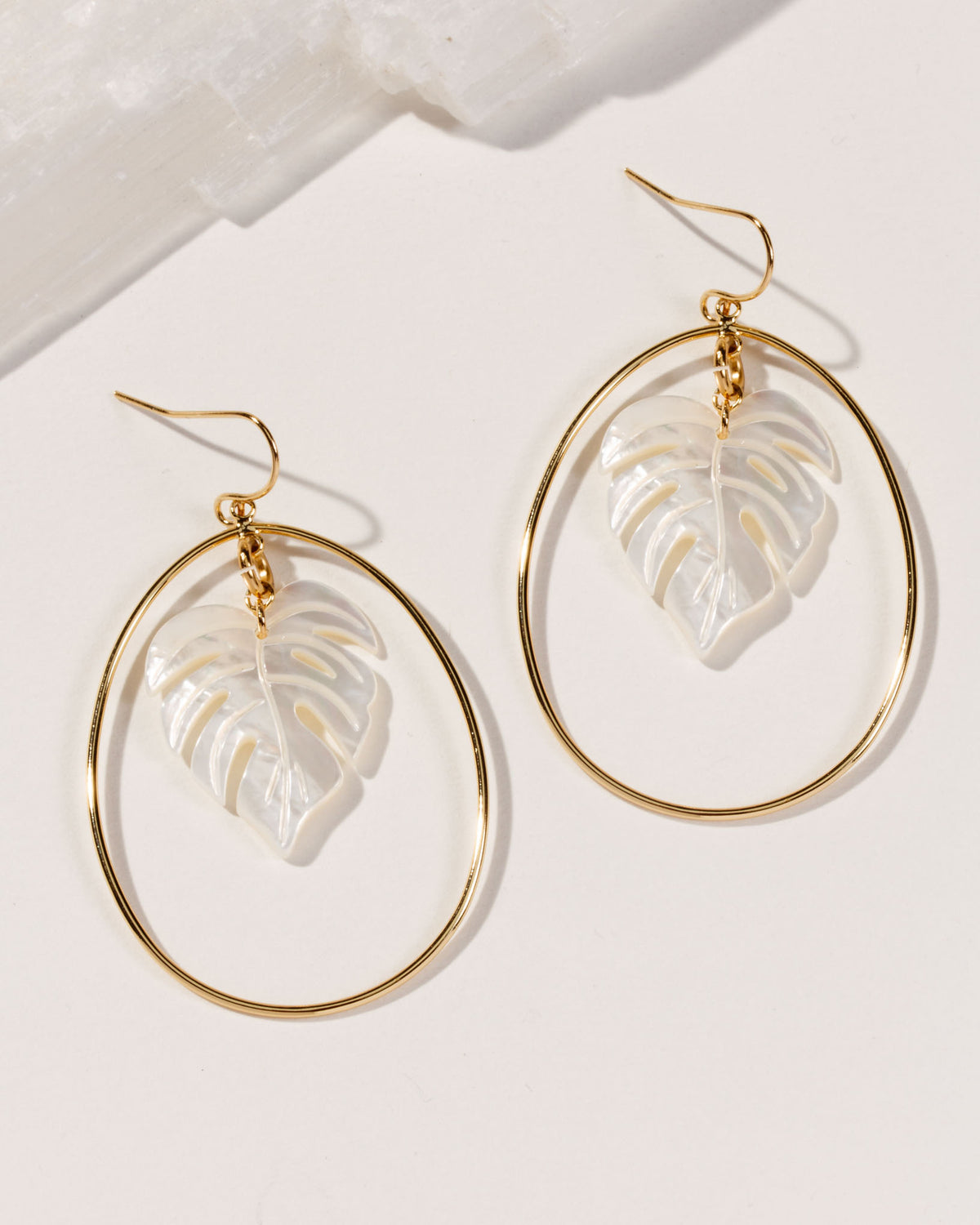 14 Karat Gold-plated hoop earrings with mother of pearl leaf-shaped cutouts on a white table