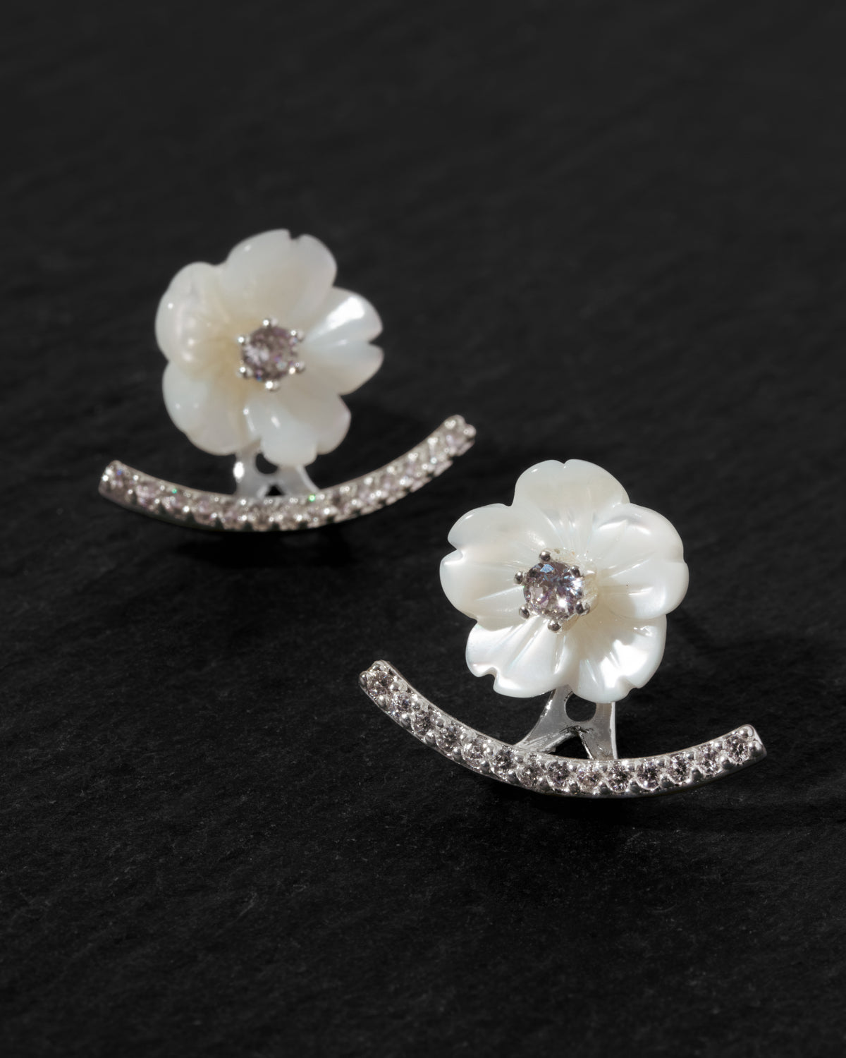 A pair of white mother-of-pearl flower stud earrings with silver clear CZ accented front back earring jacket.