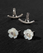 A pair of white mother-of-pearl flower stud earrings with clear CZ centers and a matching clear cz front back earring jacket, arranged on a dark textured background.