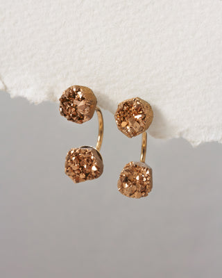 Pair of gold earrings with rose gold gemstones on a textured surface