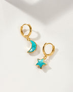 A pair of gold hoop earrings, one with a crescent moon and the other with a star, both featuring a bright turquoise blue center.