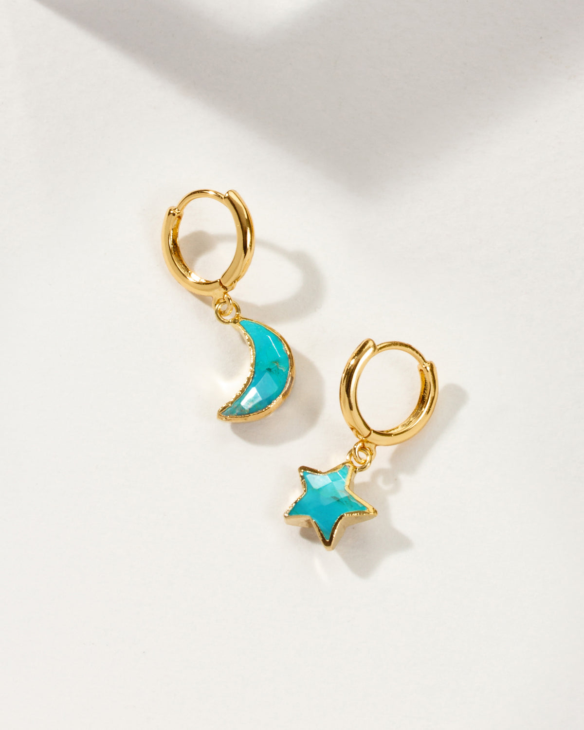 A pair of gold hoop earrings, one with a crescent moon and the other with a star, both featuring a bright turquoise blue center.