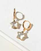 A pair of gold hoop earrings with dangling star-shaped charms made of clear quartz.