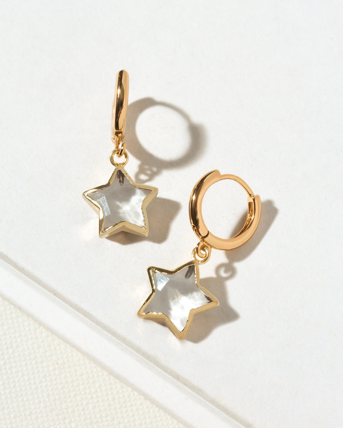 A pair of gold hoop earrings with dangling star-shaped charms made of clear quartz.
