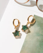 A pair of gold hoop earrings with dangling star-shaped emerald gemstone charms.