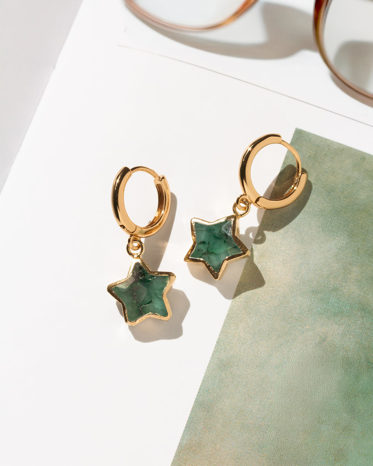 A pair of gold hoop earrings with dangling star-shaped emerald gemstone charms.