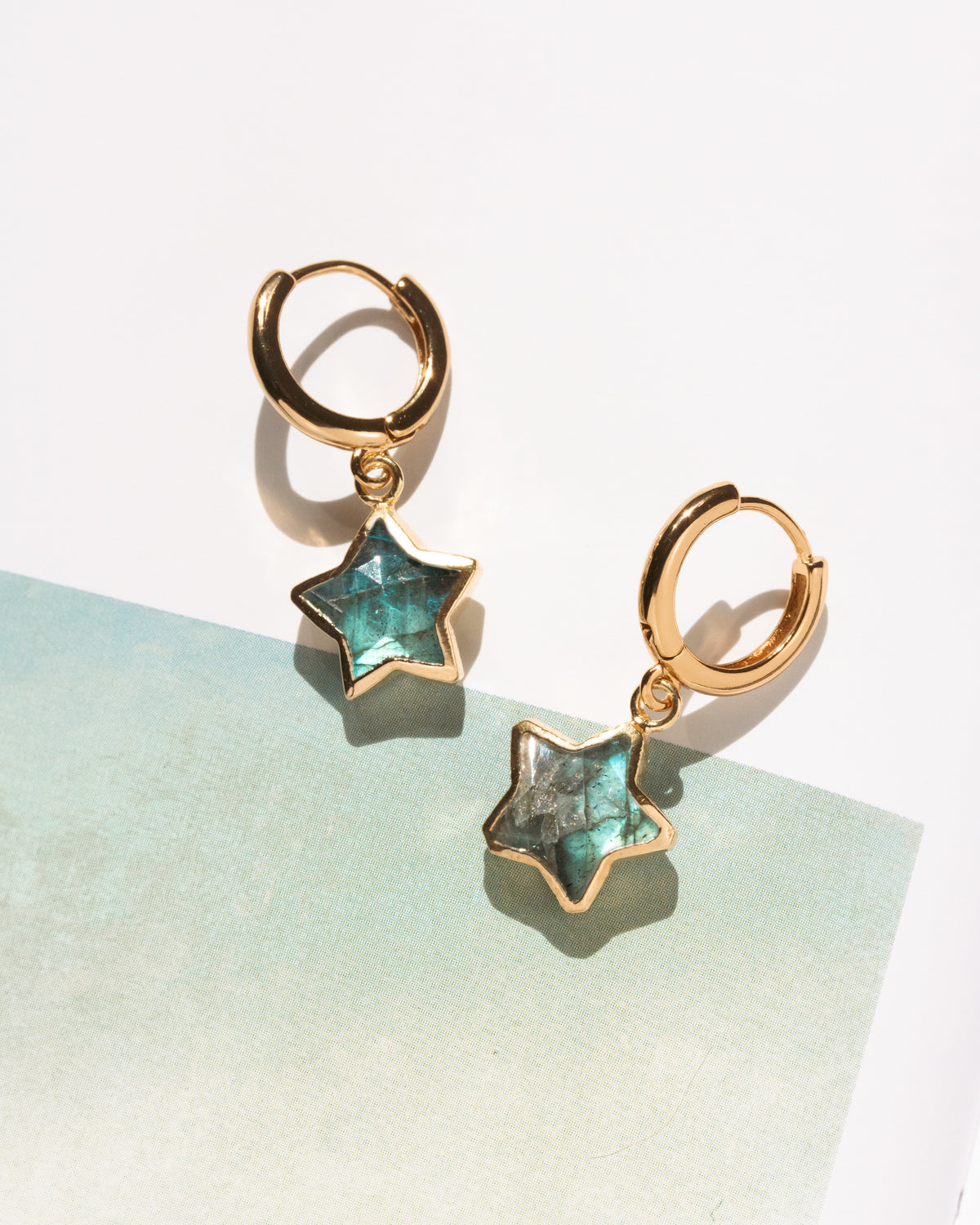 A pair of gold huggie hoop earrings with dangling faceted labradorite star charms.
