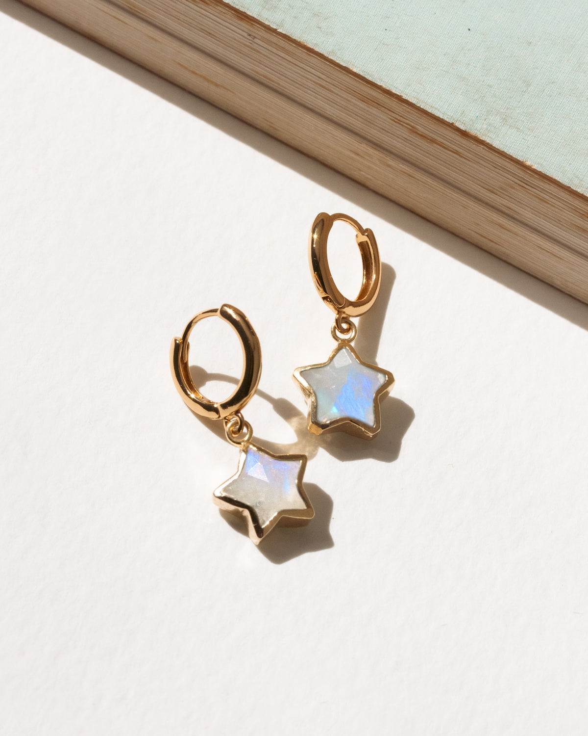 A pair of gold hoop earrings with dangling star-shaped moonstone stones.