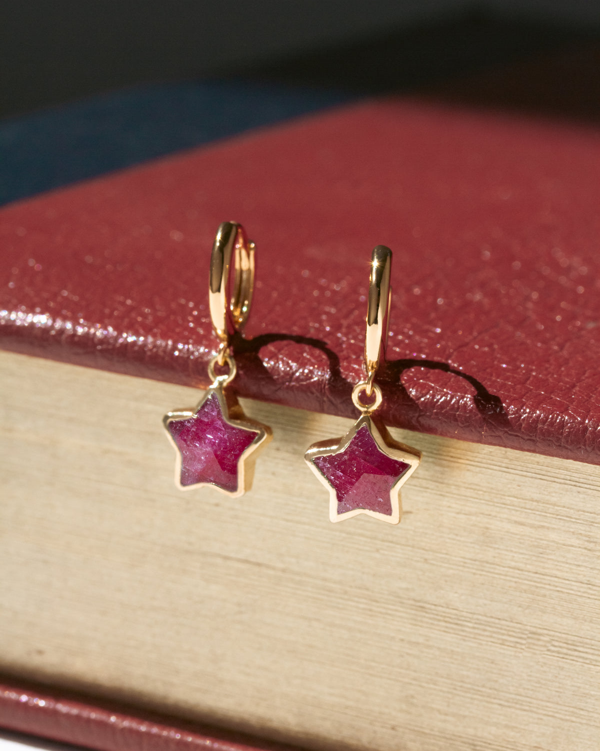 A pair of gold star-shaped drop earrings with deep pinkish-red ruby stones.