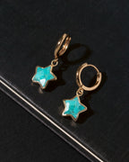 A pair of gold hoop earrings with dangling star-shaped turquoise stones.
